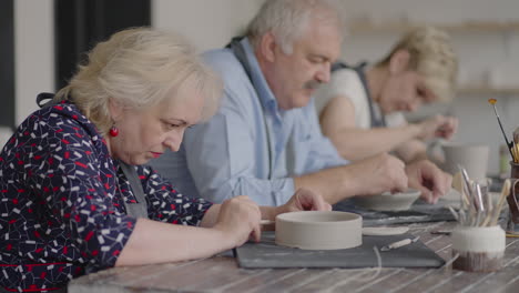 A-group-of-elderly-people-at-a-master-class-in-pottery-together-sculpt-and-cut-a-drawing-on-cups-of-clay-for-the-manufacture-of-ceramic-dishes